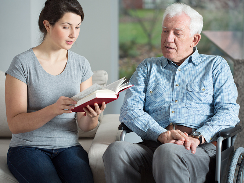 Senior care assistant reading book elderly man